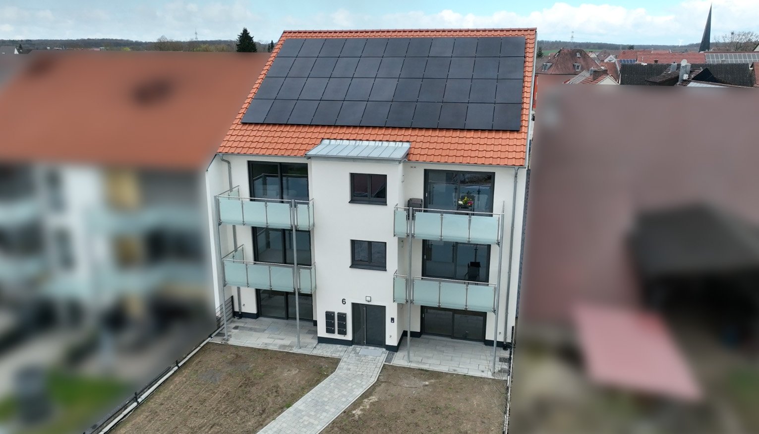Drohnenaufnahme des Neubau-Mehrfamilienhauses in der Region Schweinfurt mit schwarzer Aufdach-Photovoltaikanlage und Balkonen; benachbarte Gebäude datenschutzkonform unkenntlich gemacht.