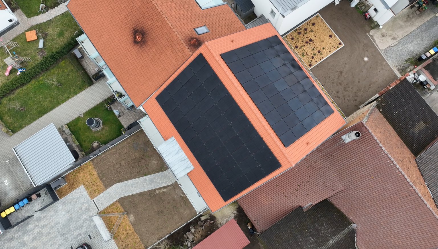 Senkrechte Drohnenaufnahme des Satteldachs mit der schwarzen Photovoltaikanlage des Mieterstrom-Projekts in der Region Schweinfurt.